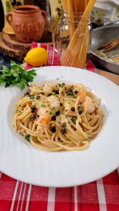 a plate of pasta with shrimp and capers on the table next to lemons