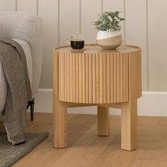 a wooden table with a coffee cup on it next to a gray chair and potted plant