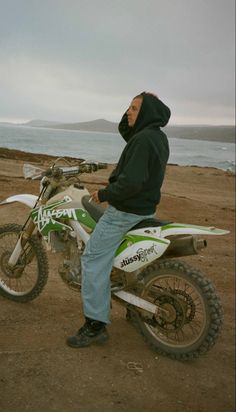 a man sitting on top of a dirt bike next to the ocean in front of him