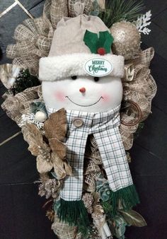 a christmas wreath with a stuffed snowman wearing a green hat and scarf on it