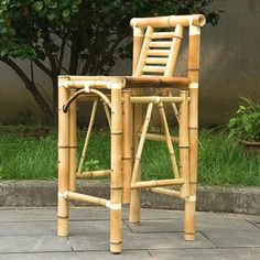 a bamboo chair sitting on top of a stone floor next to a tree and bushes