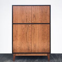 a wooden cabinet sitting on top of a cement floor next to a white wall with black trim