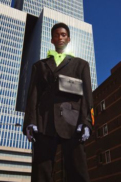 a man standing in front of a tall building wearing a black suit and yellow shirt