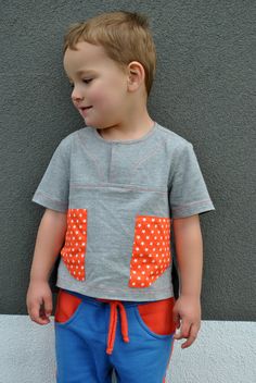 a little boy standing in front of a wall wearing blue and orange pants with polka dots on them