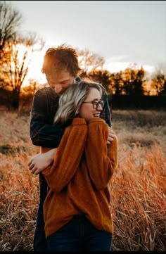 a man and woman hugging in the middle of a field with tall grass at sunset