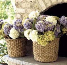 three baskets filled with purple and white flowers sitting on a stone ledge next to a brick oven