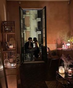 two people are sitting in the doorway of an apartment at night with candles lit on the floor