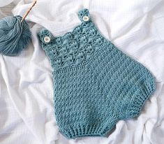 a blue crocheted baby romper laying on top of a bed next to a ball of yarn