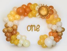 balloons arranged in the shape of a wreath with one written on it and an orange sun