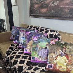 there are many disney princess dolls on the couch in front of the pictures and paintings