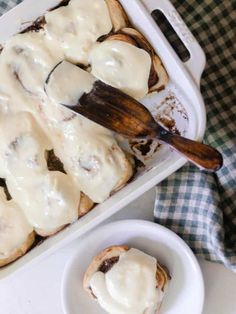 a pan filled with cinnamon rolls covered in white icing next to a wooden spoon