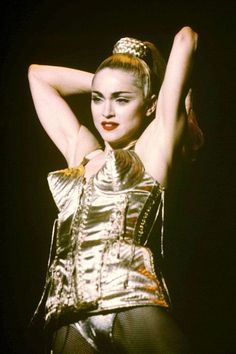 a woman with her arms behind her head wearing a silver outfit and holding her hair in the air