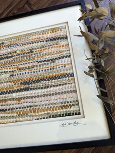 a close up of a framed artwork on a wooden floor next to a plant with leaves