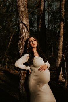 a pregnant woman leaning against a tree in the woods