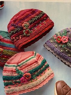 four knitted hats sitting next to each other on a blue tablecloth with a pair of brown shoes