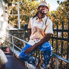 a man with dreadlocks sitting on a rail next to a fence and smiling