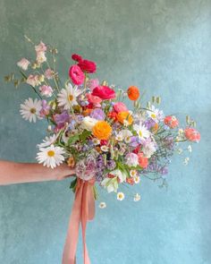 a person holding a bouquet of flowers with pink ribbon around the bottom and white daisies on top