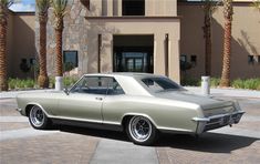 an old car is parked in front of a large building with palm trees around it