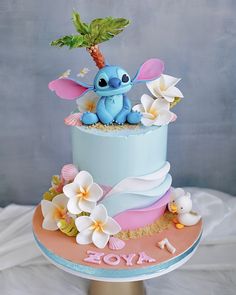 a blue and pink cake decorated with flowers, leaves and a small dragon on top