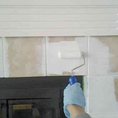 a person in blue gloves painting a wall with white paint on the walls and a fireplace