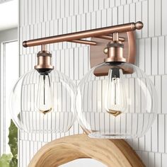 two clear glass globe lights hang from the wall above a wooden shelf in a bathroom