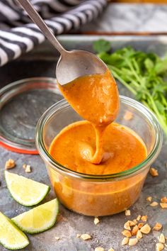 a spoon full of sauce being lifted from a glass bowl with limes and cilantro on the side