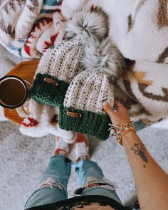 a person holding a coffee cup in their hand while sitting on the floor with two knitted hats