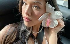 a woman sitting in the back seat of a car holding a flower up to her face