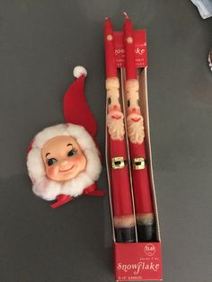 two red candles with santa claus's face on them next to a christmas ornament