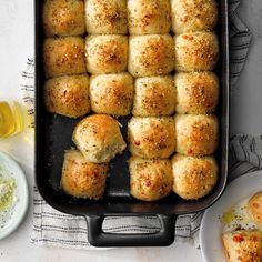 a pan filled with rolls covered in cheese and seasoning next to plates of dipping sauces