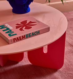 a pink table with a book on it and a blue vase filled with flowers in the background