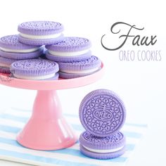 purple cookies are stacked on top of each other in front of a pink cake stand