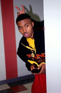 a young man standing in front of a wall holding his hand up to the side