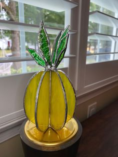 a yellow glass vase sitting on top of a wooden table next to a windowsill