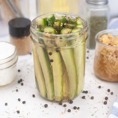 a jar filled with cucumbers sitting on top of a table next to spices