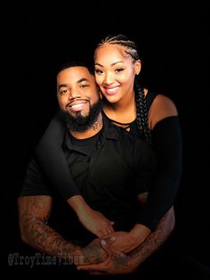 a man and woman are posing for a photo in front of a black background with their arms around each other