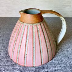 a pink and white ceramic pitcher sitting on top of a carpeted floor next to a wall