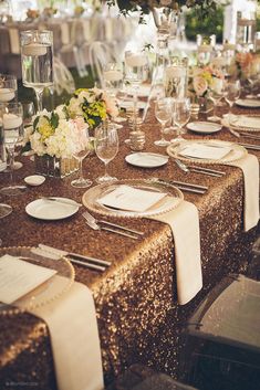 the table is set with white and gold linens, silver place settings, and floral centerpieces