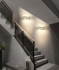 a vase with flowers sitting on top of a table next to a stair case and light fixture