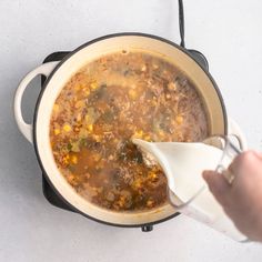 a person pouring milk into a pot filled with soup on top of a white counter