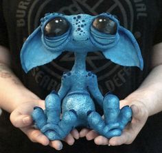 a person holding out their hands with blue paint on it and an alien like creature in the middle