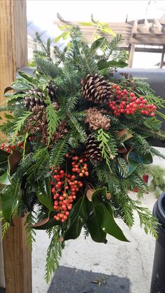 a christmas wreath with pine cones and berries hanging from it's centerpiece on a post