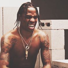 a man with dreadlocks and tattoos on his chest sitting in front of a wall