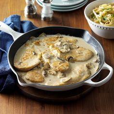 a skillet filled with chicken and mushrooms on top of a wooden table next to bowls of salad