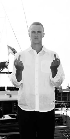 a man standing in front of a boat giving the peace sign with both hands and holding up two fingers