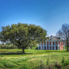 an old house sits in the middle of a green field with trees and grass around it