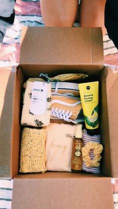 a box filled with lots of items sitting on top of a bed next to someone's legs