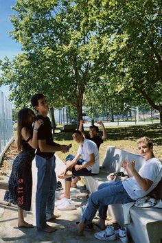 a group of people sitting and standing next to each other on a bench under a tree