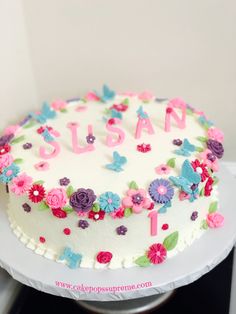 a white cake with flowers and butterflies on it sitting on a table next to a sign that says susan