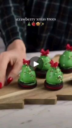 a person is decorating small green christmas trees on a wooden board with red bows